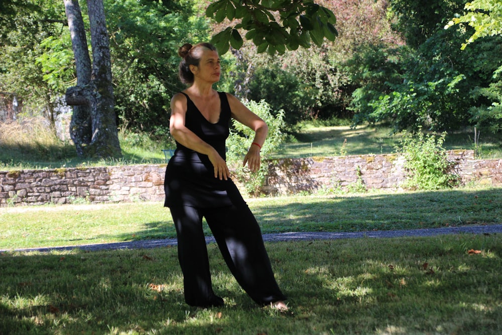 woman in black tank top and black pants standing on green grass field during daytime