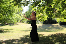 A serene woman practicing gentle movement outdoors surrounded by mossy greenery.