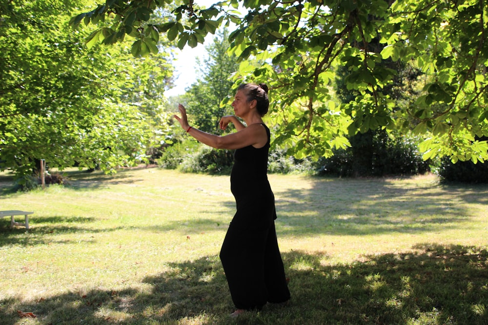 femme en robe noire sans manches debout sur le champ d’herbe verte pendant la journée