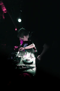 A DJ spinning vinyl records under moody purple and gold lighting in a cozy club.