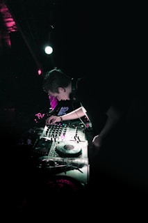 A DJ performing in a dark club illuminated by neon lights.