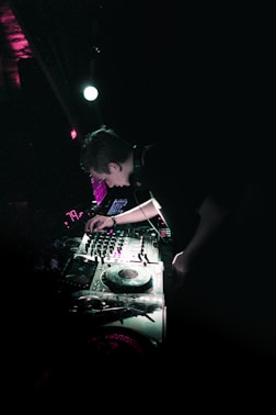 A DJ performing live with vibrant urban light effects surrounding him.