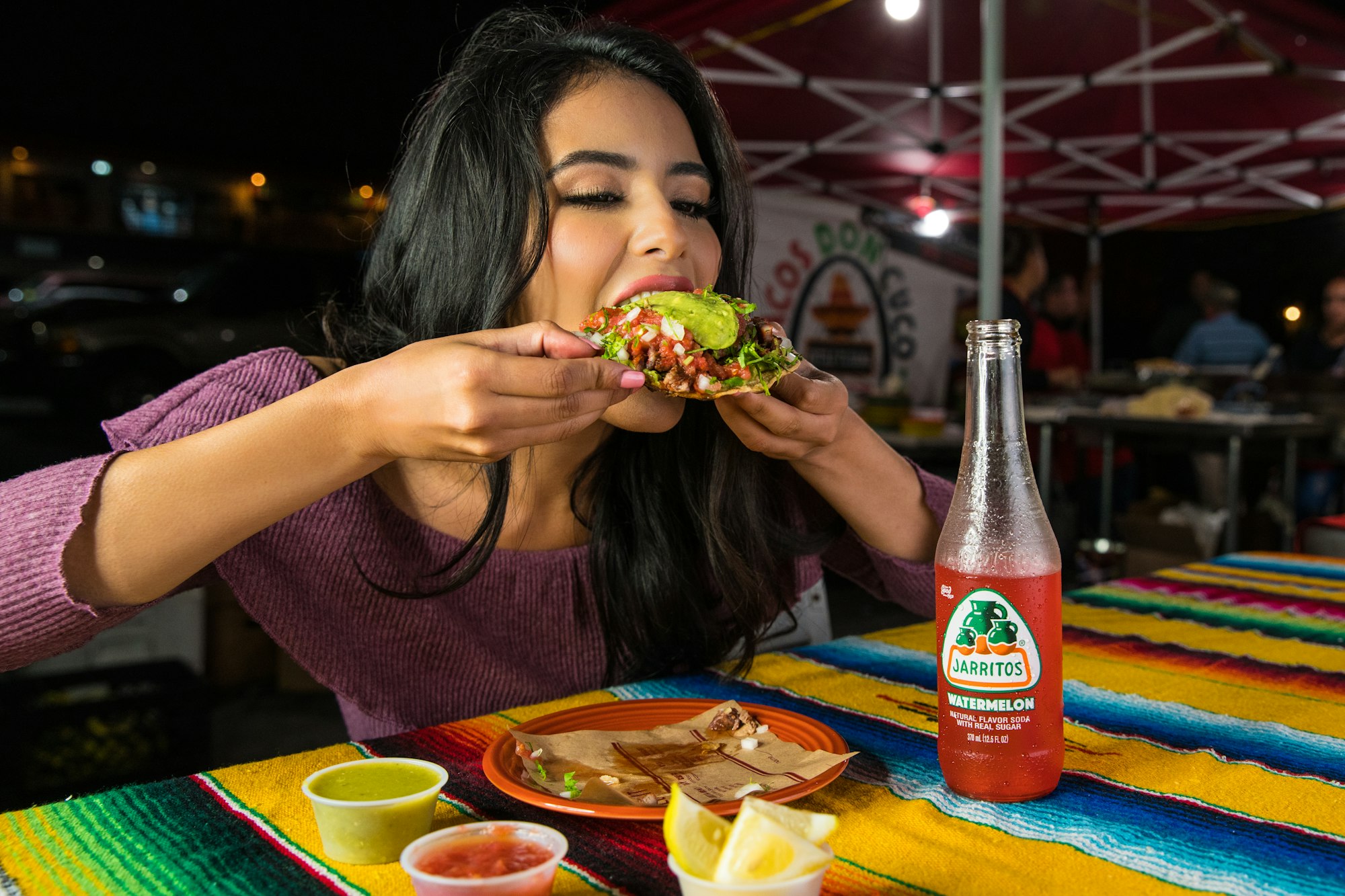 A woman eats a tostada at a street taco stand in Los Angeles at night.