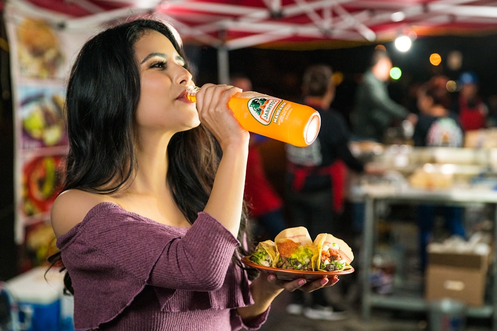 woman in purple long sleeve shirt drinking orange juice