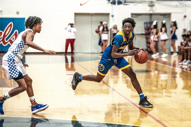 A dynamic basketball game moment featuring players in black and gold uniforms under bright gym lights.