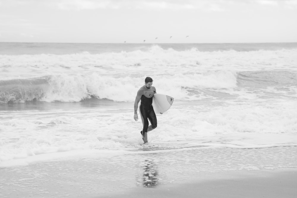 man in black wet suit holding white surfboard walking on beach during daytime