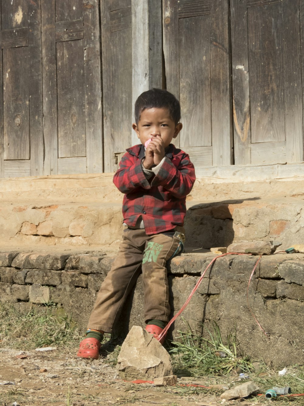 boy in brown and green camouflage jacket and brown pants sitting on brown rock during daytime