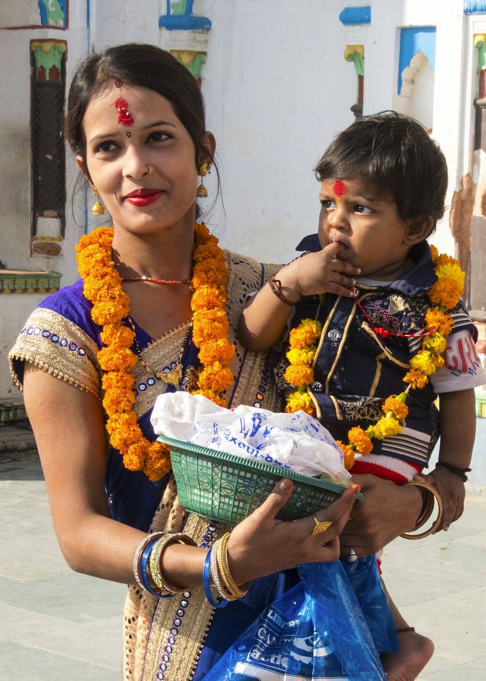 woman in blue and white floral sleeveless dress carrying a baby in green basket