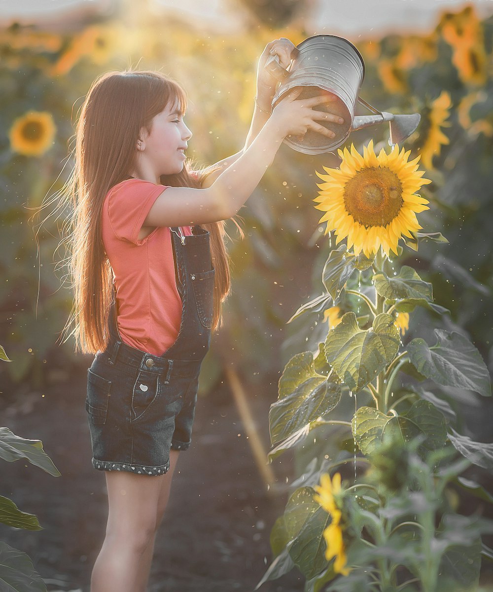 woman in orange tank top and black denim shorts holding sunflower during daytime