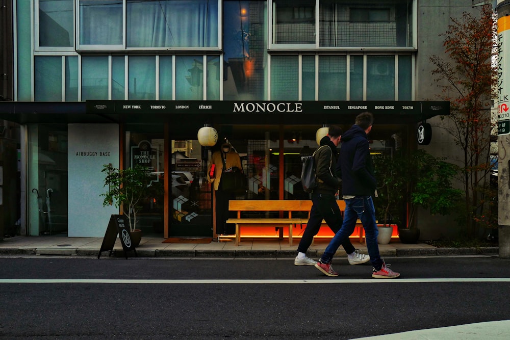 Uomo in giacca nera e jeans di jeans blu che cammina sul marciapiede durante il giorno