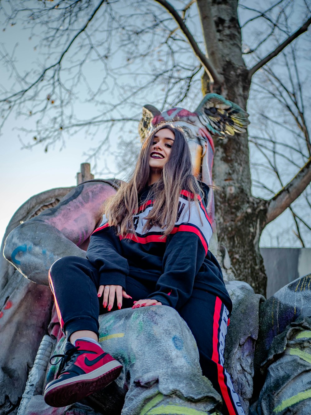 woman in black and red jacket sitting on tree branch during daytime