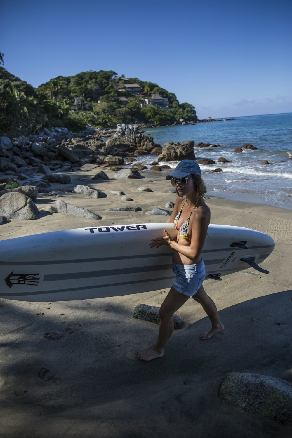 woman in blue denim shorts standing on white surfboard on beach during daytime