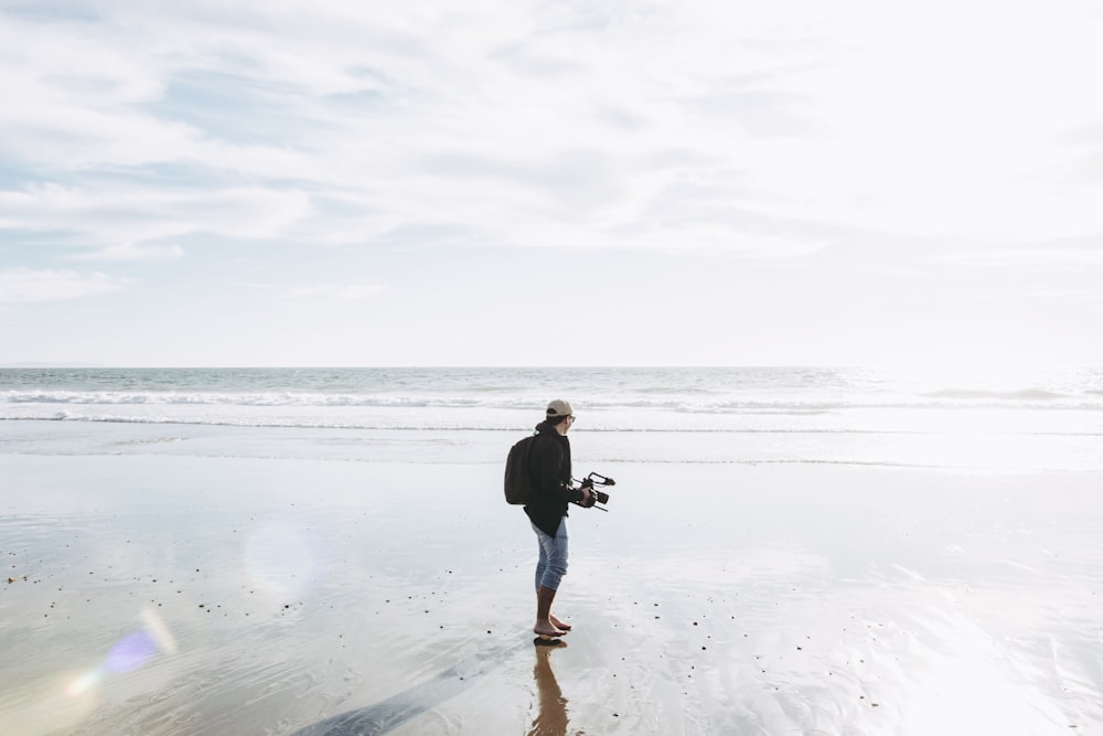 man in black jacket and blue denim jeans holding black dog on beach during daytime