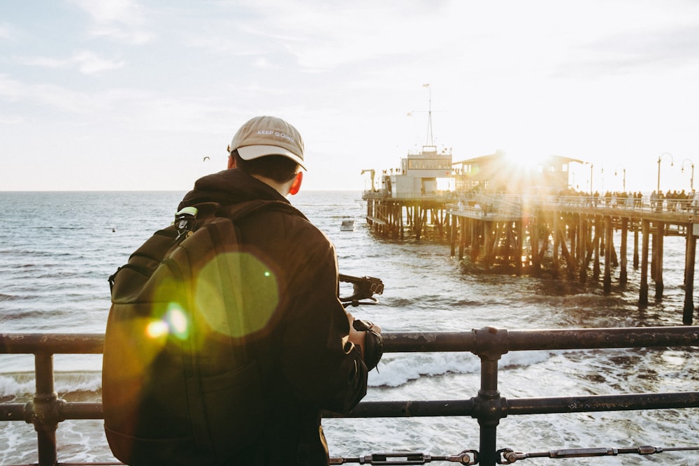 man in black jacket and white cap holding black fishing rod near body of water during