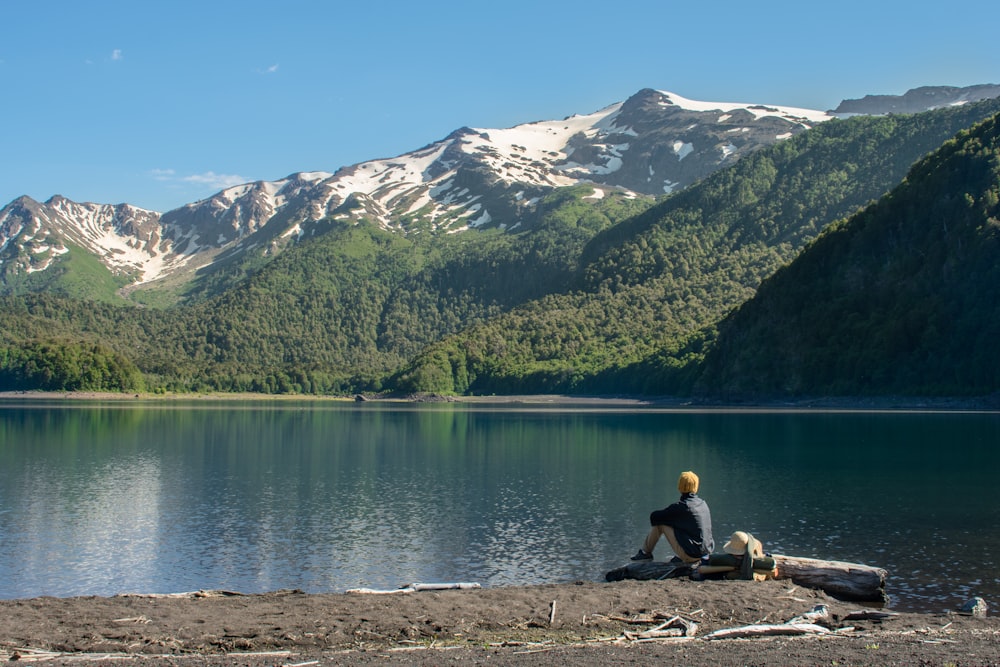 2 people sitting on rock near lake and mountain range
