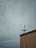 A cloudy sky looms over a building with a satellite dish installed on the edge. The building's wall shows signs of age with visible cracks. The atmosphere seems heavy and overcast, suggestive of an impending storm.