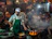 A bustling street food market at night featuring a cook in a green apron and white cap, tending to a flaming stove with several frying pans. Surrounding him are diners seated at tables, enjoying meals. Red lanterns are hanging above, while steam and smoke fill the air, creating an energetic and lively atmosphere.