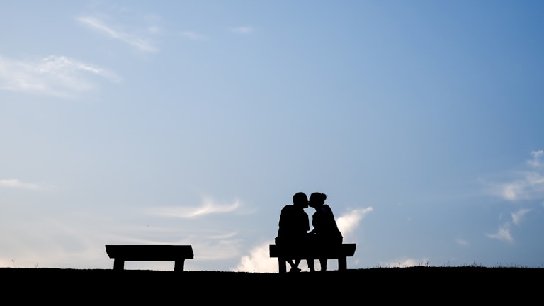 a photo showing a silhouette of 2 person sitting on bench during sunset