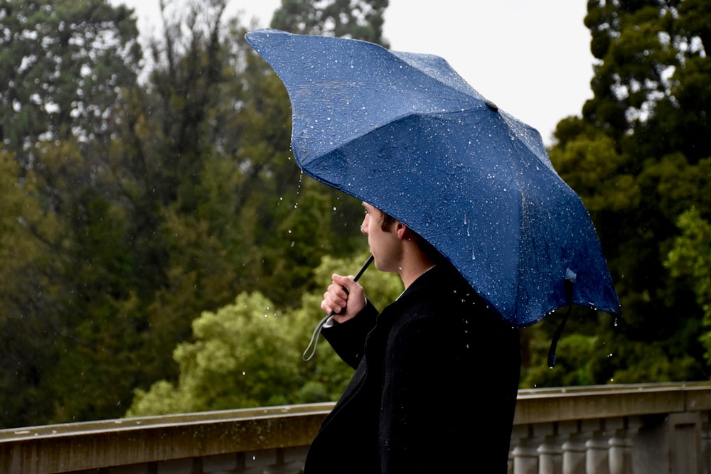 person in black coat holding blue umbrella