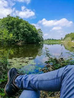 A serene lakeside scene with someone meditating quietly, eyes closed, surrounded by calm water and trees.
