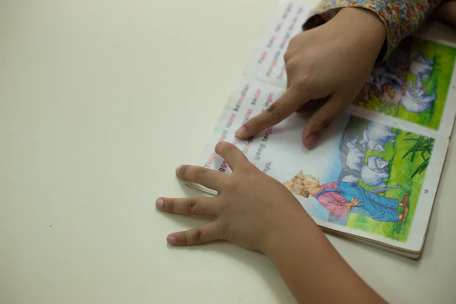 Hands of different ages and backgrounds holding open books with illustrated stories.