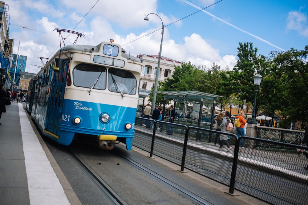 Menschen, die tagsüber auf der Straße in der Nähe der blau-weißen Straßenbahn gehen