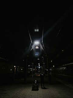 A cozy backpack resting on a worn wooden bench at a bustling train station, with a cityscape blurred in the background.