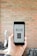A person is holding a smartphone displaying an app with buttons labeled Scan, Cart, and History against a blurred brick wall background. The app interface appears to be minimalistic and functional.