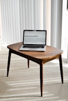 A laptop is placed on a small wooden table in a room with light-colored carpet and vertical blinds. The laptop screen displays a webpage titled 'Interactive RFID', indicating a focus on technology.