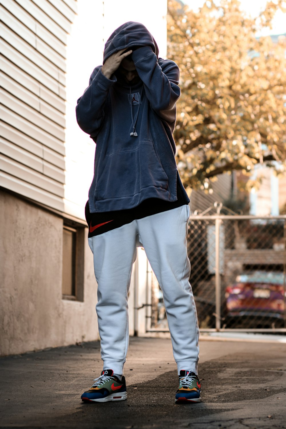 man in gray hoodie and white pants standing near gray steel fence during daytime