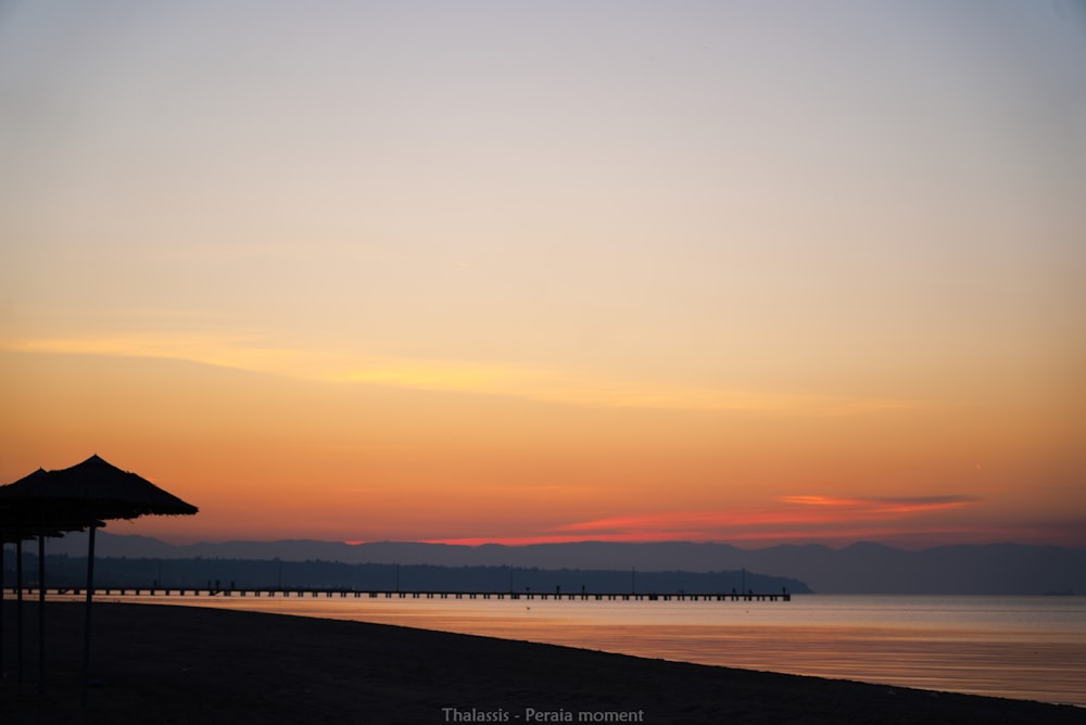 silhouette of person standing on seashore during sunset