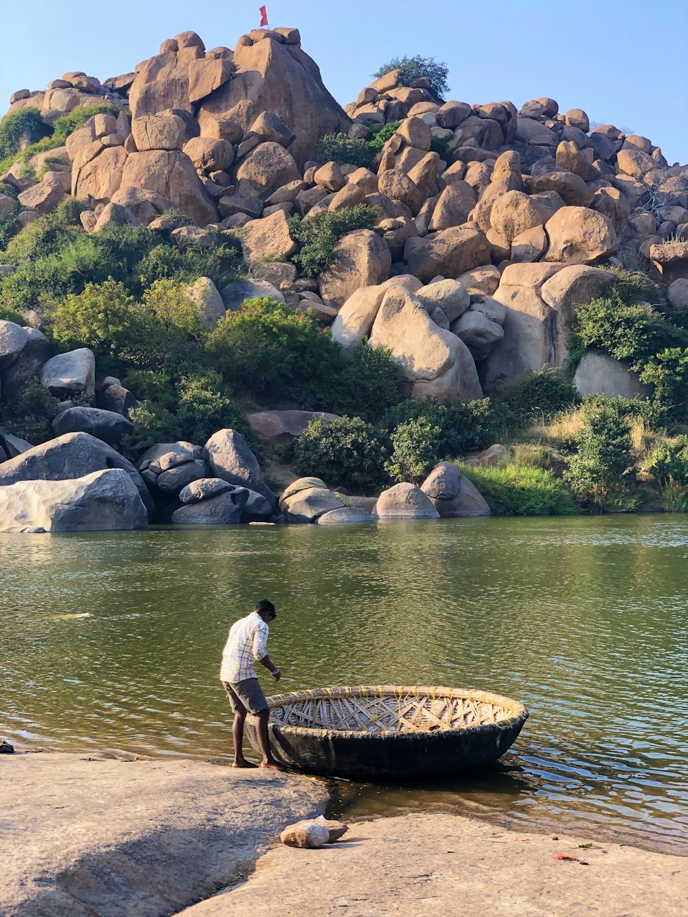 man in white shirt and black shorts standing on brown rock near body of water during