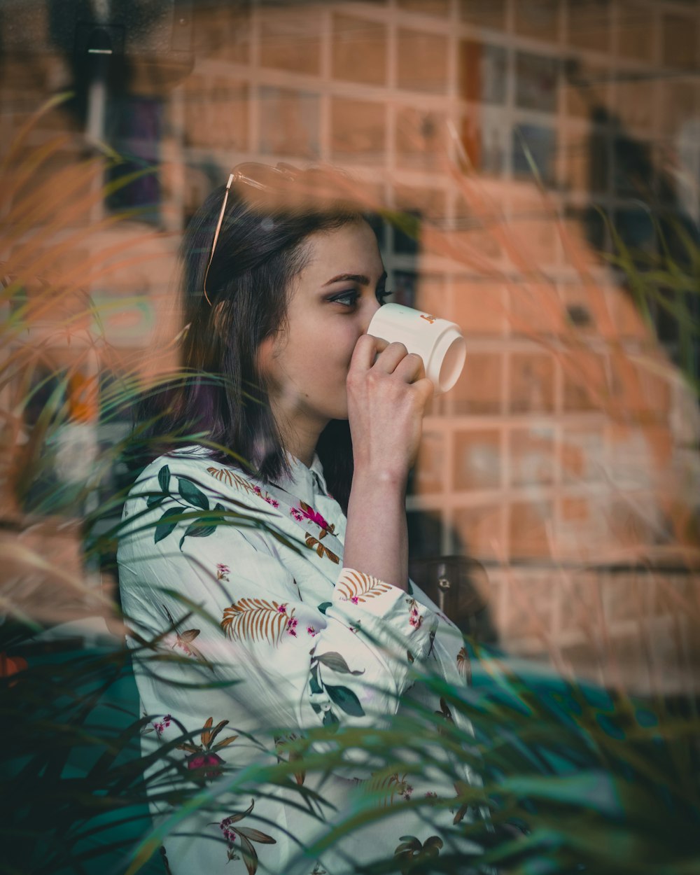 woman in white and red floral shirt drinking from white ceramic mug