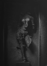 A detailed stone sculpture of a figure adorned with intricate jewelry and clothing, captured in low light. The artwork displays expertly carved intricate details, creating a sense of ancient artistry.