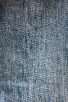 Close-up view of blue denim fabric with a textured pattern, showing the weave and stitching details.
