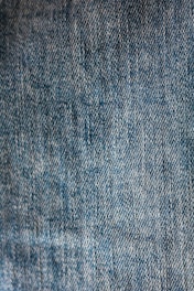 Close-up view of blue denim fabric with a textured pattern, showing the weave and stitching details.