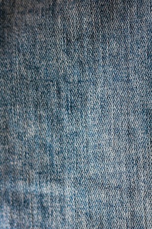 Close-up view of blue denim fabric with a textured pattern, showing the weave and stitching details.