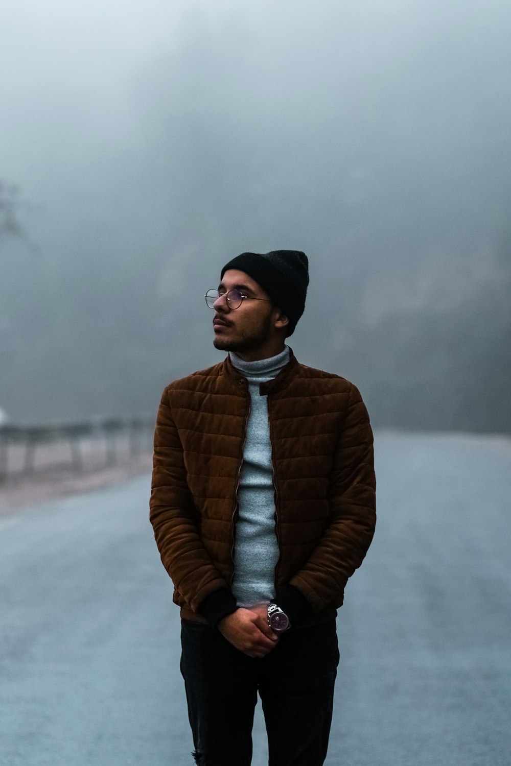 man in brown jacket and black knit cap standing on road during daytime