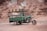 A green motorcycle rickshaw is parked in front of a rocky, eroded cliff. The vehicle has a fringed canopy adorned with a floral pattern that adds a decorative touch to the utilitarian design.