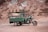 A green motorcycle rickshaw is parked in front of a rocky, eroded cliff. The vehicle has a fringed canopy adorned with a floral pattern that adds a decorative touch to the utilitarian design.