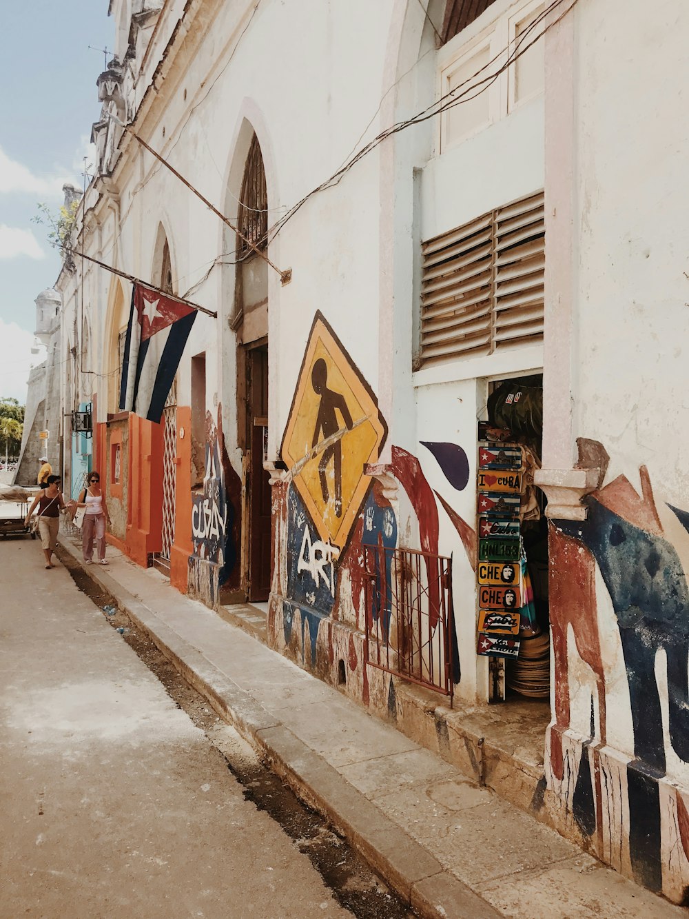 man in white t-shirt and black pants standing beside wall with graffiti during daytime