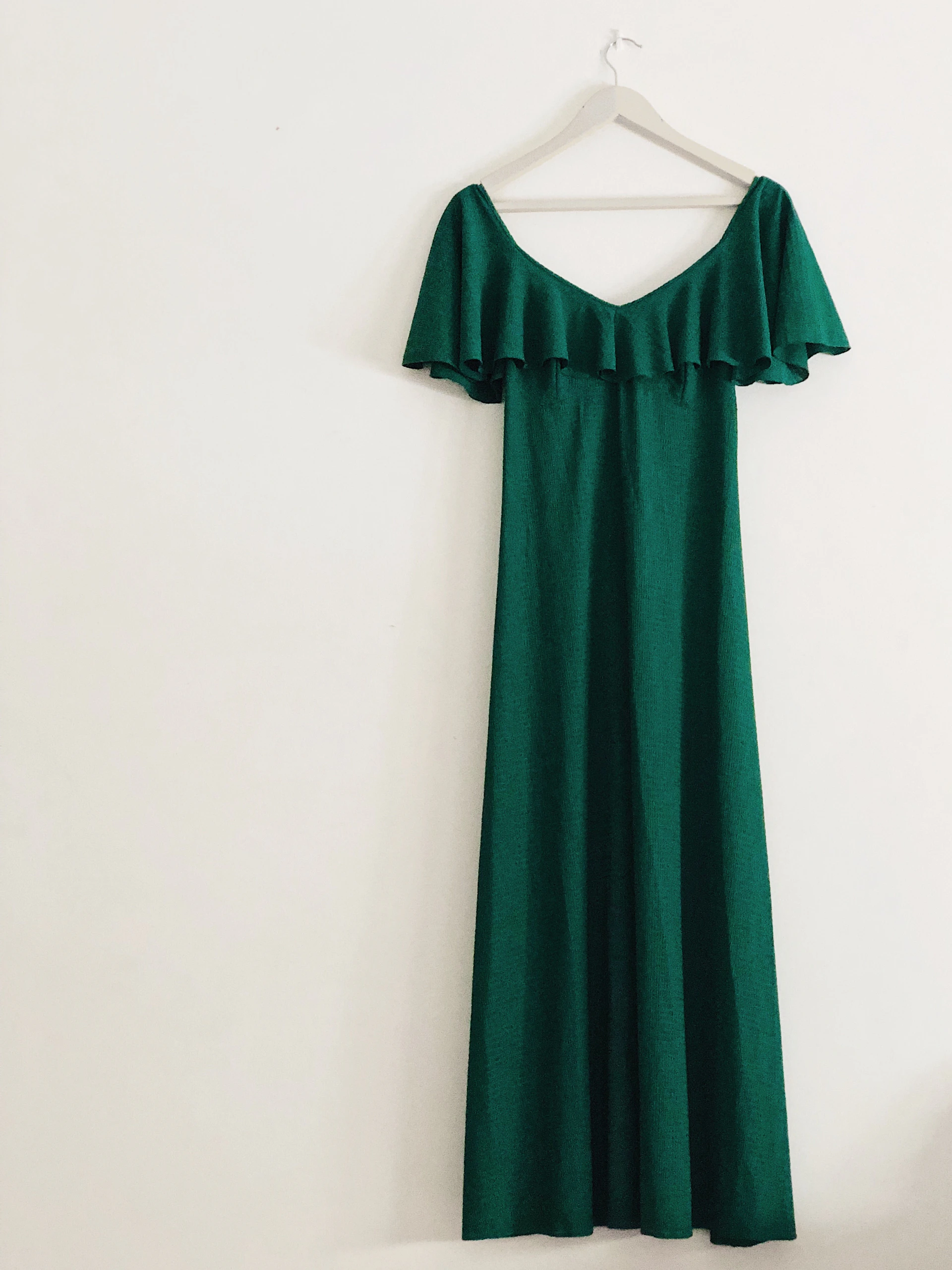 An elegant emerald green mini dress featuring clean lines, hanging on a minimalist white rack with natural light highlighting its texture.