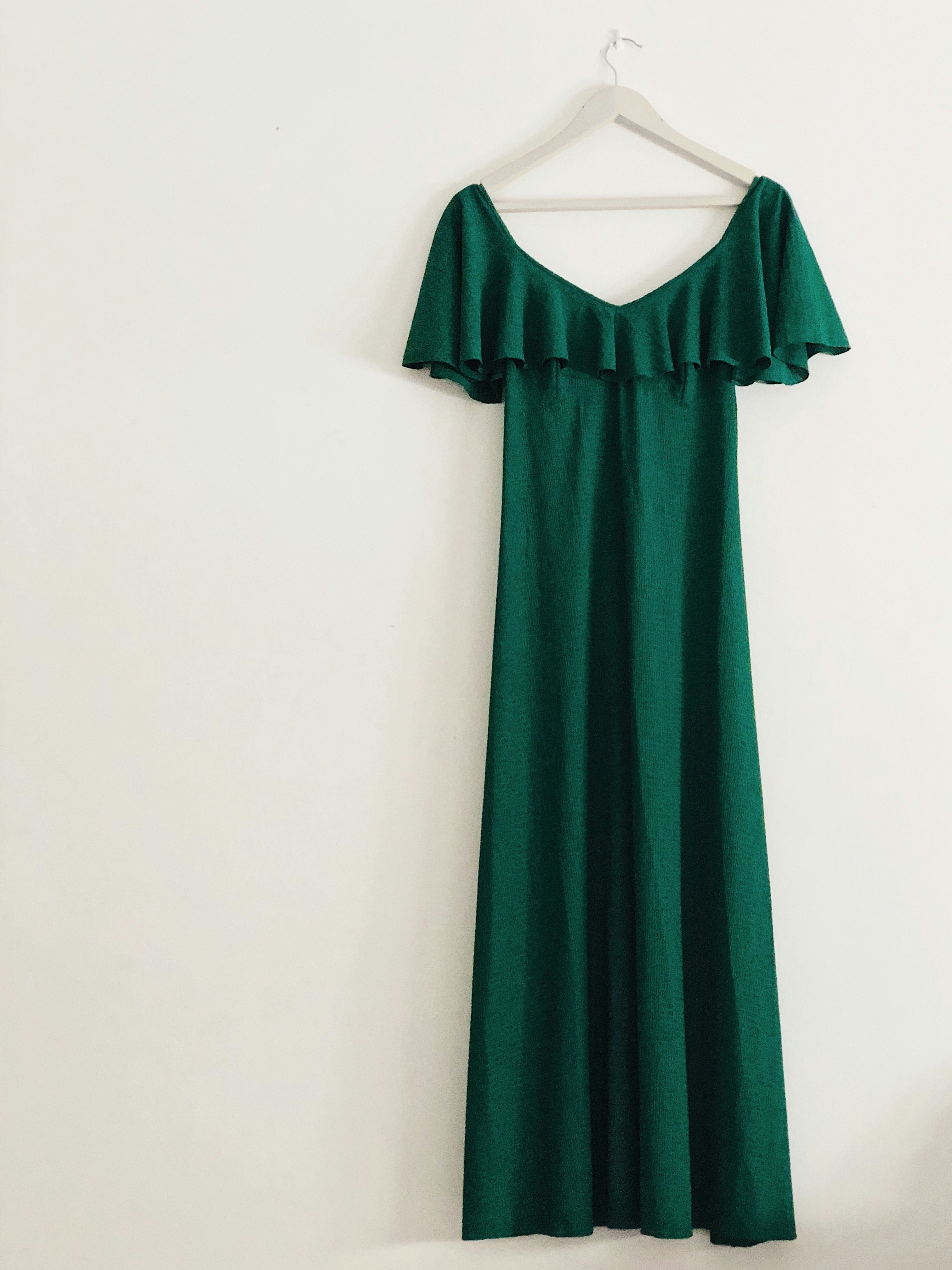 A beautiful long green dress on a hanger on a white wall 