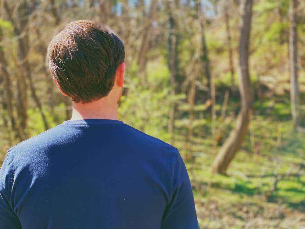 man in blue crew neck shirt standing in forest during daytime