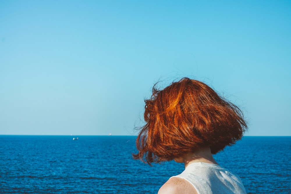 Frau im weißen Hemd schaut tagsüber auf das Meer