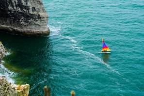 A vibrant pirate ship with black and red sails sailing on turquoise Mediterranean waters under a sunny sky.
