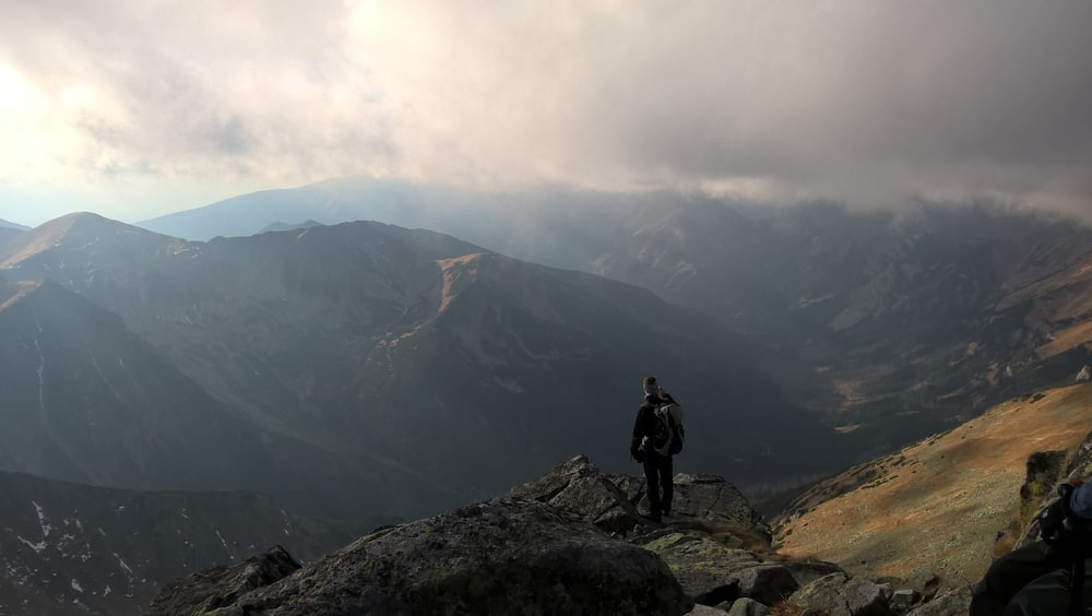 man in black jacket standing on rock mountain during daytime