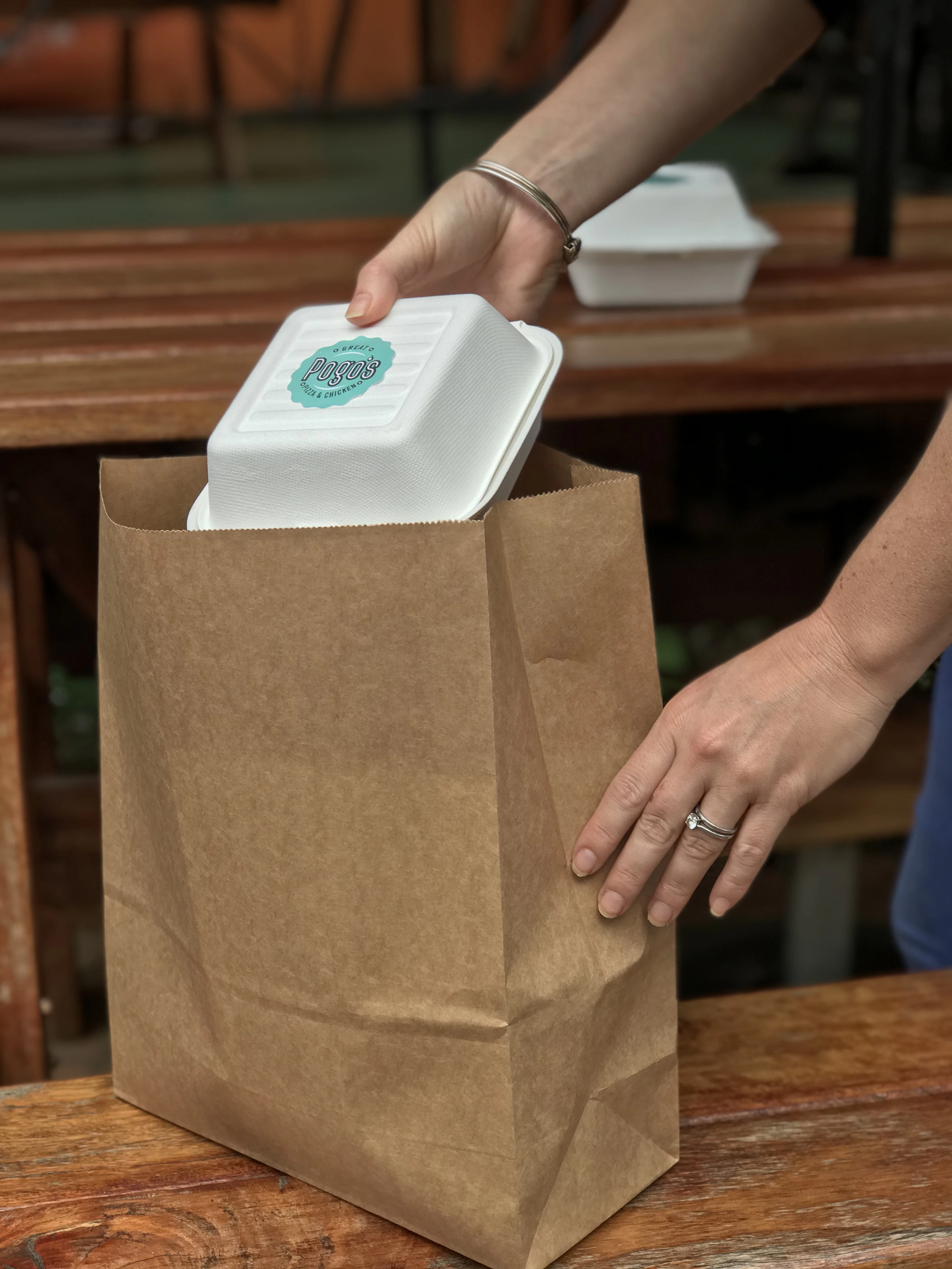 A takeaway clamshell being packed into a kraft paper bag on a timber counter