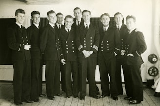 A group of cadets in crisp uniforms standing proudly on the deck of a training vessel under clear blue skies.