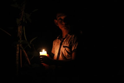 man in white and black button up shirt holding lighted candle frightened teams background